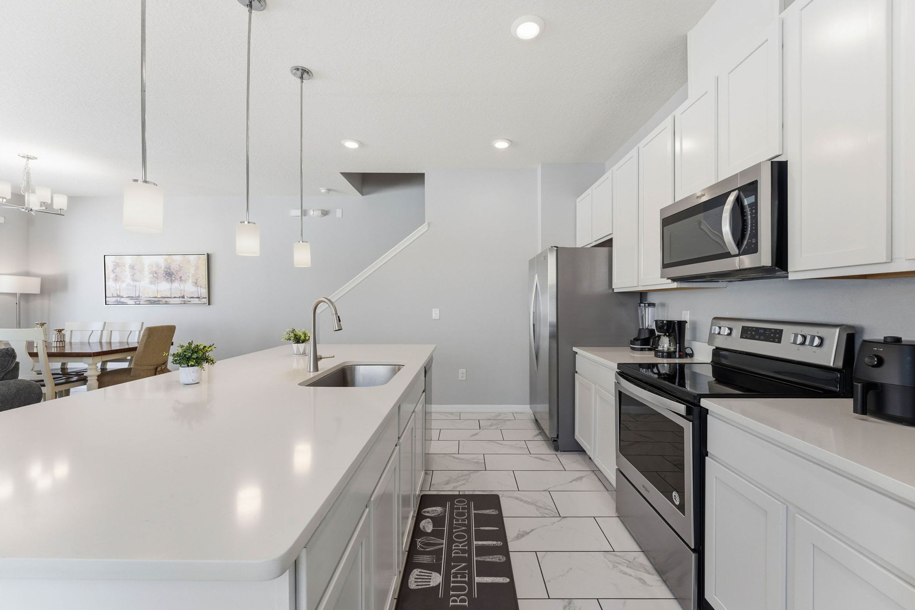A modern kitchen with white cabinetry, stainless steel appliances, and pendant lighting.