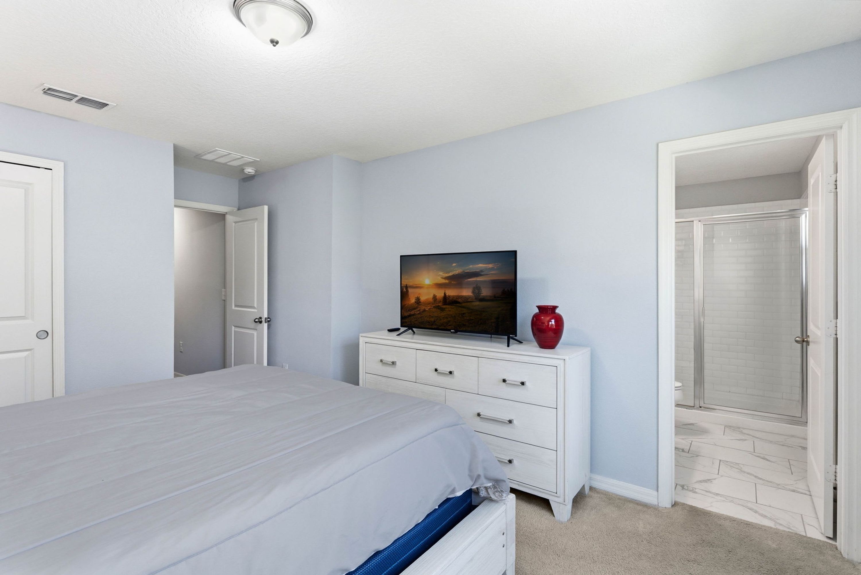 A bedroom with a bed, a dresser, a television, and a red vase.