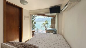 Quarto com cama, televisão na parede e vista para uma varanda com mesa e cadeiras.