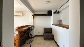 Um espaço pequeno com um balcão de madeira e dois bancos, uma cadeira estampada e uma estante com um objeto decorativo.