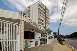 A hotel entrance with a modern design, including a glass facade and a prominent sign. - Apto com lazer completo a 500m da Praia da Enseada (Bertioga)