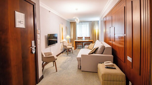 A hotel room with a wooden door, a television, a sofa, a small table, and a lamp. - Apto no Brasil 21 - Conforto e Localização Central (Brasilia)