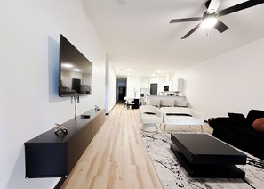 Ein modernes Wohnzimmer mit Flachbildfernseher an der Wand, Deckenventilator und Holzboden.