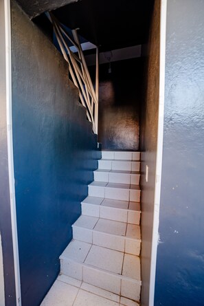 A staircase with white steps and a wooden handrail, leading to a dark interior space. - Flat com Wi-Fi próximo ao Aeroporto (Fortaleza)