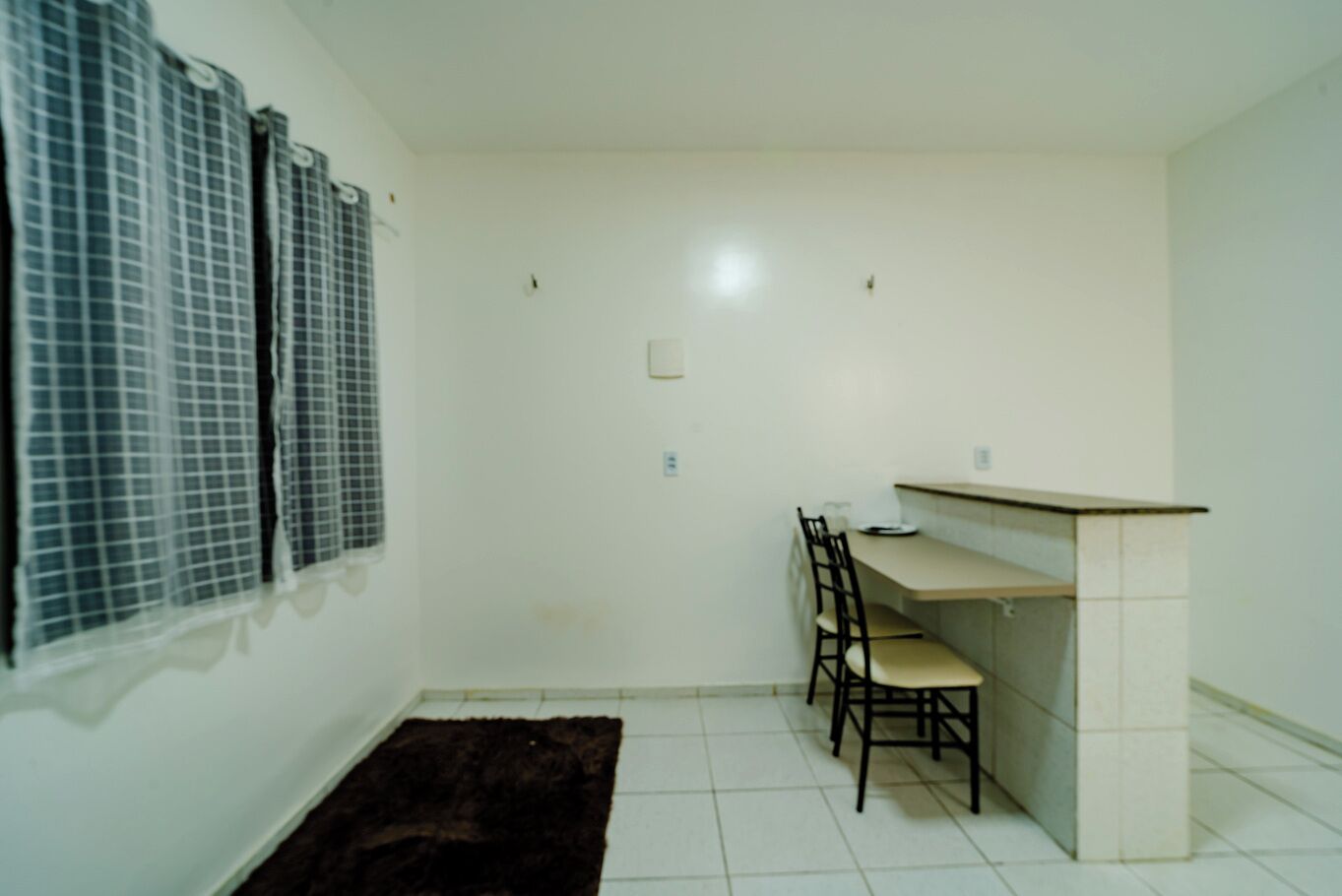 A small, clean room with a single dining table and chairs, a dark rug, and a window with blinds.