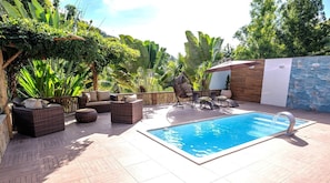 A poolside area with wicker furniture, a small pool, and lush greenery.