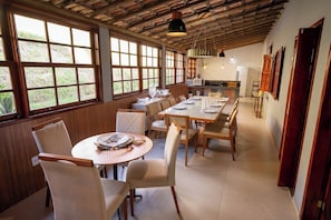 A spacious dining area with large windows, wooden ceiling beams, and a long table set for dining.