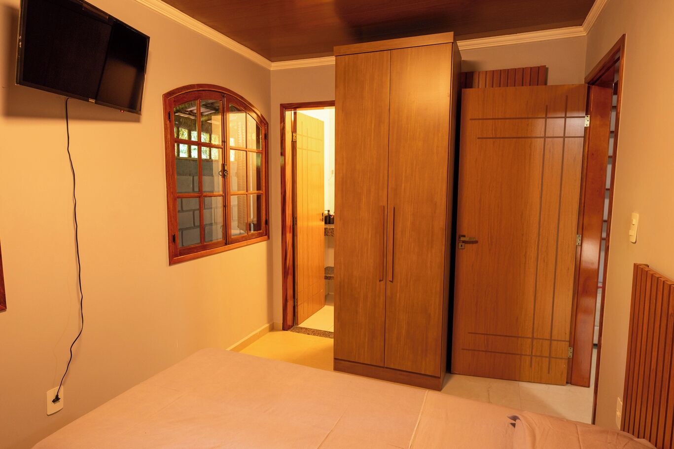 Een slaapkamer met een bed, een aan de muur bevestigde televisie, houten kasten en een raam met uitzicht.