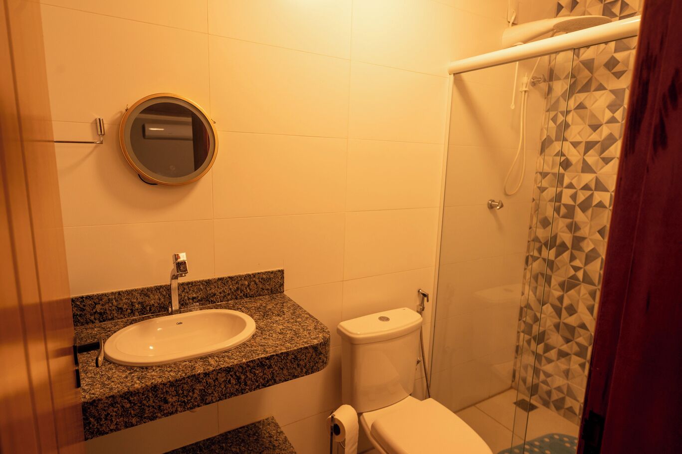 Ein Badezimmer mit Marmorwaschtisch, Toilette und Dusche mit geometrischen Fliesenmustern.