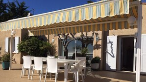 A patio with a table and chairs, a potted plant, and a building with striped awning and shutters.