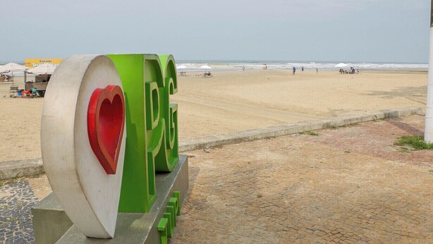 Blick auf einen Strand mit einem großen, grün-weißen Schild, das ein Herzsymbol und die Buchstaben „PG“ zeigt.