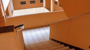 Eine Treppe mit Handlauf, die zu einer oberen Etage mit gefliestem Boden und Fenstern führt.
