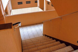 Eine Treppe mit Handlauf, die zu einer oberen Etage mit gefliestem Boden und Fenstern führt.
