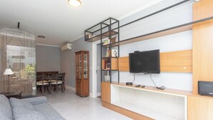Una sala de estar moderna con un sofá gris, un aparador de madera, un televisor y un comedor con sillas y una mesa.