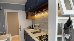 Una cocina compacta con armarios azul oscuro, una encimera blanca y una estufa a gas.