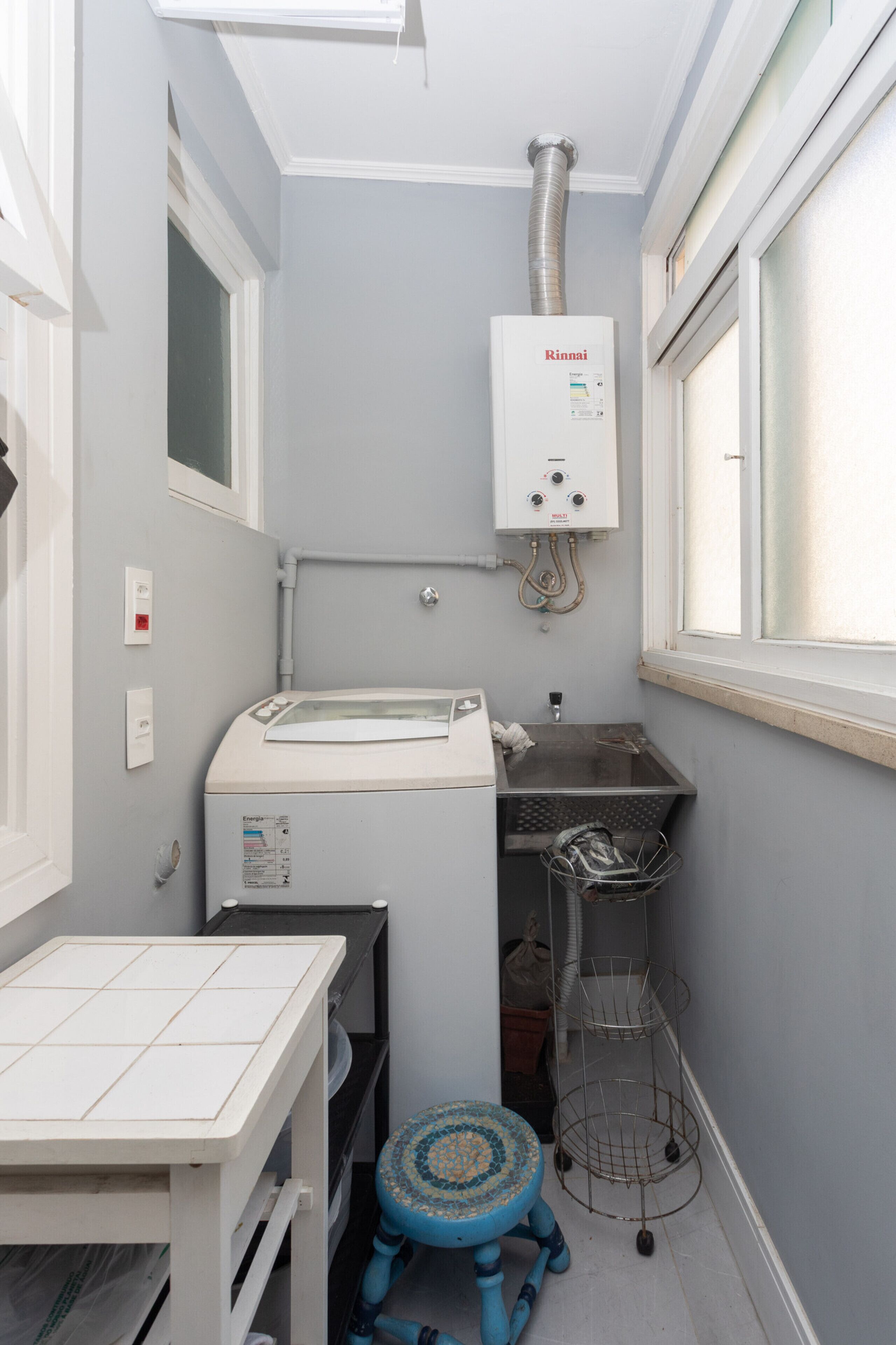 A compact bathroom with a white heater, a sink, and a small table with a blue stool.