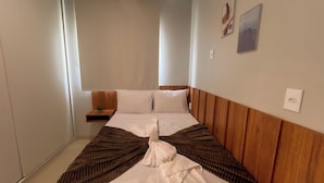 A hotel room with a bed, a bedside table with a plant, and a wall-mounted outlet. - Apto c 2 suítes e Lazer Completo a 100m da Praia (Japaratinga)