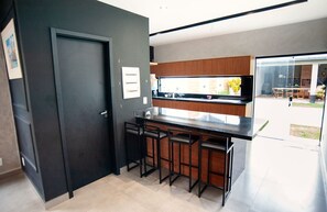 A modern kitchen with a dark door, wooden cabinets, a black countertop, and three bar stools. - Casa pet friendly c piscina, churrasqueira e wi-fi (Saquarema)