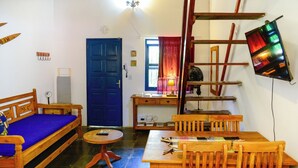 Ein gemütliches Wohnzimmer mit blauer Tür, Holzmöbeln, einem kleinen Tisch und einem an der Wand montierten Fernseher.