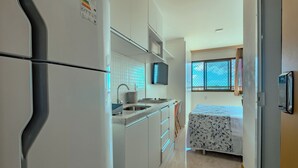 Eine kompakte Küche mit Kühlschrank, Spüle und Mikrowelle. Im angrenzenden Raum befindet sich ein Bett mit einem blumigen Bettüberwurf.