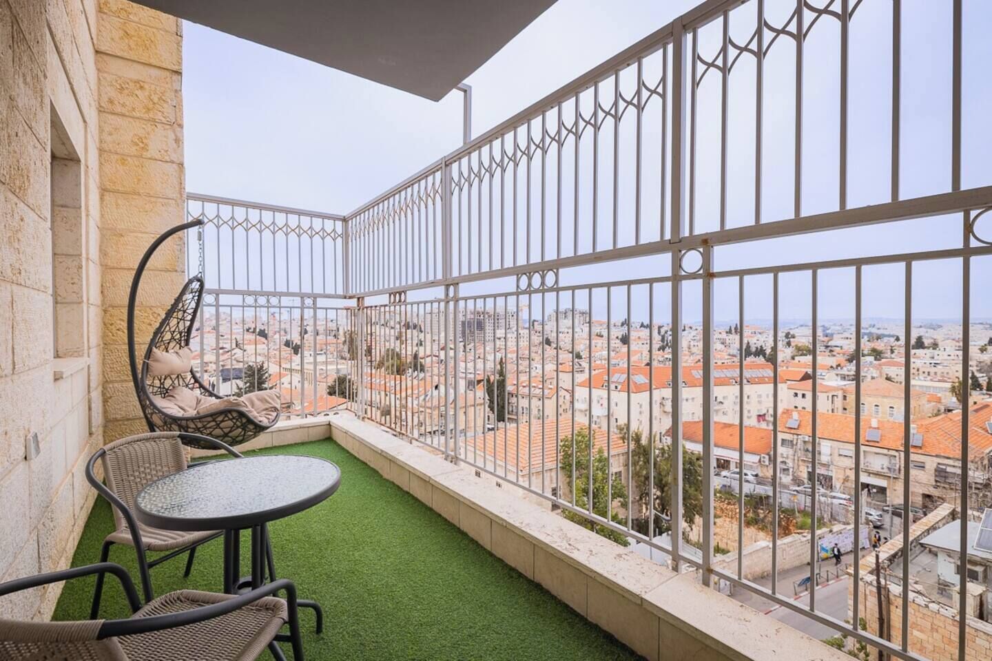 A balcony with a view of a cityscape, a hanging chair, and a small round table.