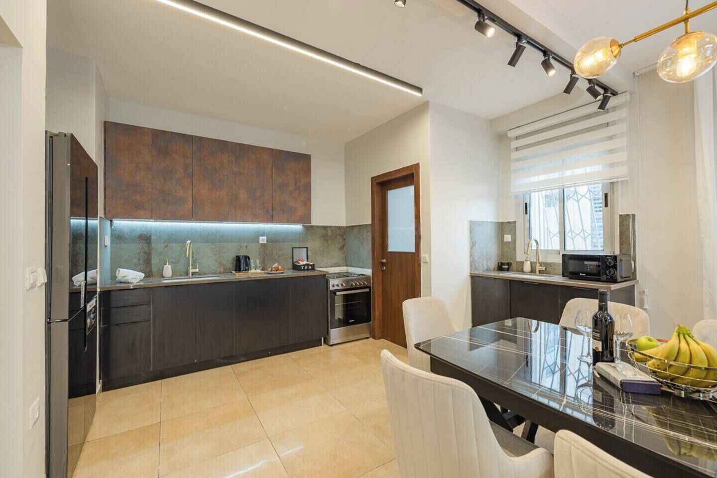 A modern kitchen with dark cabinetry, a built-in oven, and a dining area with a glass table and white chairs.