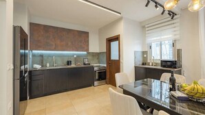 A modern kitchen with dark cabinetry, a built-in oven, and a dining area with a glass table and white chairs. - 3 BR Apartment in Yisha'ayahu (w/ safe room) (Jerusalem)