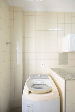 Ein kleiner Waschraum mit einer Waschmaschine mit Frontlader, einer Arbeitsplatte und einer darüber angebrachten Mikrowelle.