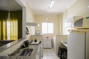 Eine kleine Küche mit Spüle, Herd, Mikrowelle und einem Fenster für Tageslicht.