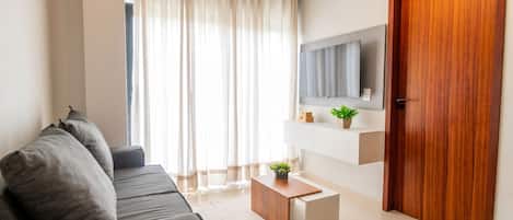 A modern living room with a grey sofa, a wooden coffee table, a flat-screen TV mounted on the wall, and a wooden door.