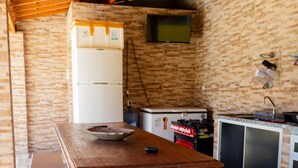 Una cuina rústica amb taula i bancs de fusta, un frigorífic, una estufa i un televisor muntat a la paret.