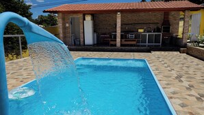 Una piscina amb una font, una zona de barbacoa i un petit edifici amb teulada de rajola.