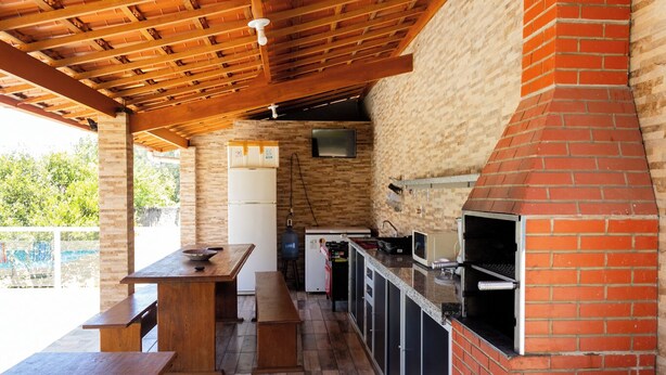 Cuina exterior amb forn de totxins, taula de fusta i nevera.
