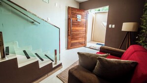 A modern living room with a staircase, a wooden door, and a red sofa. - Casa em Jacumã, com piscina, 5 suites e Fliperama (Conde)