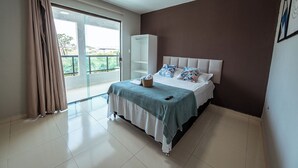 A bedroom with a bed, a wardrobe, a balcony, and a view of greenery. - Casa em Jacumã, com piscina, 5 suites e Fliperama (Conde)