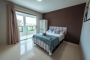 A bedroom with a bed, a wardrobe, a balcony, and a view of greenery. - Casa em Jacumã, com piscina, 5 suites e Fliperama (Conde)