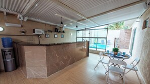 A modern kitchen with a marble countertop, a water dispenser, and a coffee machine. There is a dining area with a table and chairs, and a view of a swimming pool outside. - Casa em Jacumã, com piscina, 5 suites e Fliperama (Conde)
