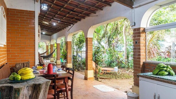 Un área de comedor al aire libre techada, con paredes de ladrillo, vigas de madera y vistas a exuberante vegetación.