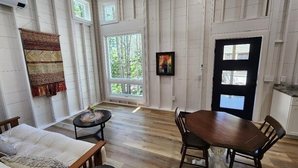 Amplia habitación con una gran mesa de madera para comer, un sofá y una pequeña mesa redonda. Cuenta con ventanas amplias que dejan entrar luz natural y vistas a zonas verdes al exterior.