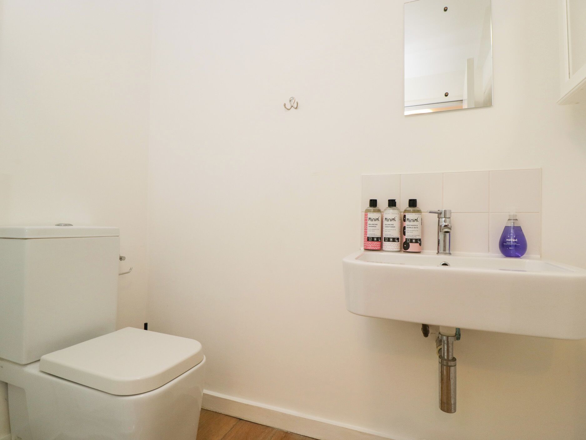 Un baño pequeño y limpio con inodoro, lavabo y tres botellas de jabón Minimpil.