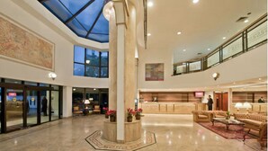 A spacious lobby with a high ceiling, a central column, and a glass ceiling. There are seating areas and a reception desk. - Flat c Academia, Sauna e Garagem - Jardim Paulista (São Paulo)