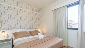 A neatly made bed with a brown blanket and pillows, a bedside lamp, and a window with curtains. - Flat c Academia, Sauna e Garagem - Jardim Paulista (São Paulo)