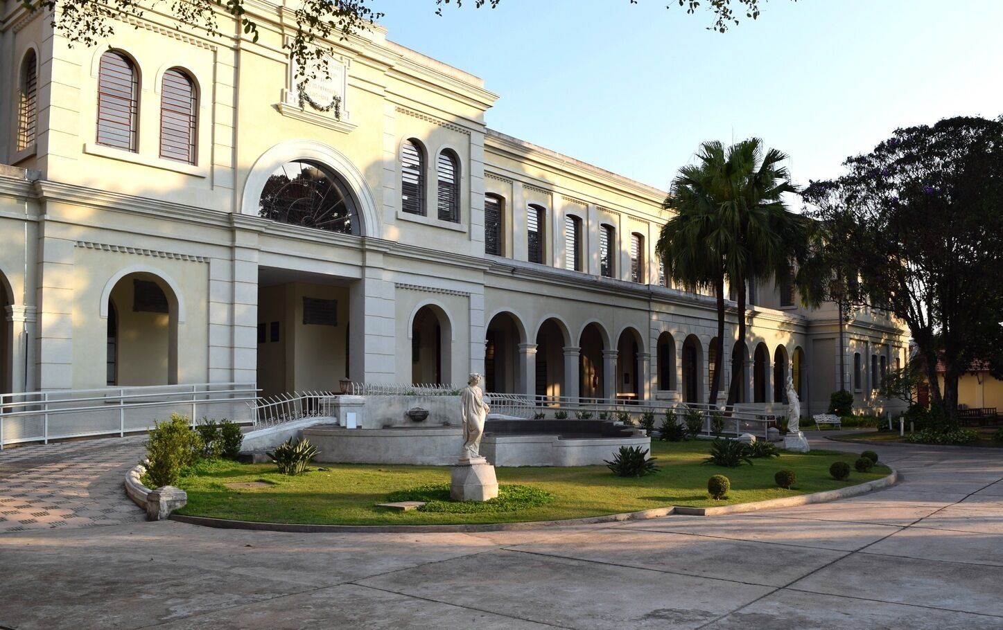 Um edifício clássico com um pátio central, apresentando uma estátua e palmeiras.