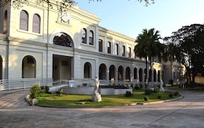 A classical building with a central courtyard, featuring a statue, palm trees, and a well-maintained lawn. - Loft com smart lock e varanda no Bresser (São Paulo)