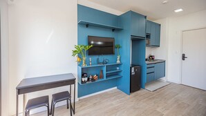 A compact living space with a kitchenette, a dining area with a table and chairs, and a TV mounted on the blue wall. - Loft com smart lock e varanda no Bresser (São Paulo)