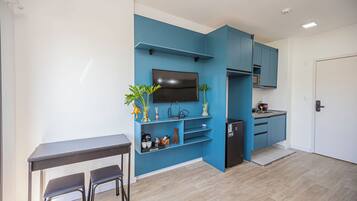 Um espaço compacto com cozinha compacta, área de refeições com mesa e cadeiras, e televisão fixada na parede azul.