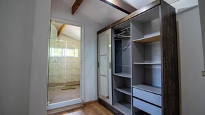 Ein Zimmer mit einer Schiebeglastür, die zu einem Badezimmer führt, einem eingebauten Kleiderschrank mit mehreren Regalen und einem Holzbalken an der Decke.