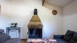 Ein Wohnzimmer mit Kaminofen, Nähmaschine auf einem Tisch und zwei Sofas.