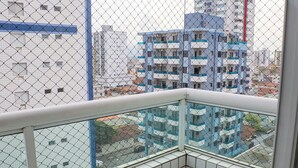 Un edificio alto con fachada azul y blanca, visto desde un balcón con cerco de malla.