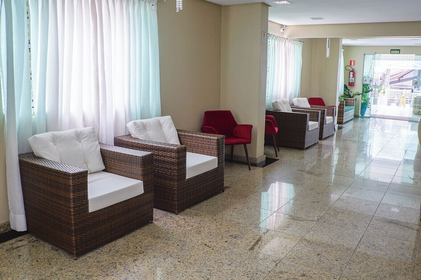 A hotel lobby with wicker chairs, a red chair, and a reception area.